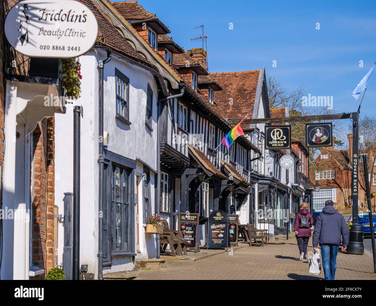 Pinner Village High Street. Historic Queen’s Head Pub, Fridolin’s Beauty Clinic, Pizza Express Old village bakery building. People walking on street. Stock Photo