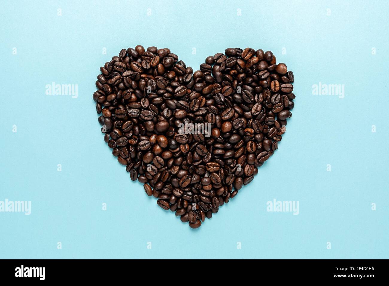 Coffee beans in shape of heart on blue background. Creative minimal coffee drink concept. Stock Photo