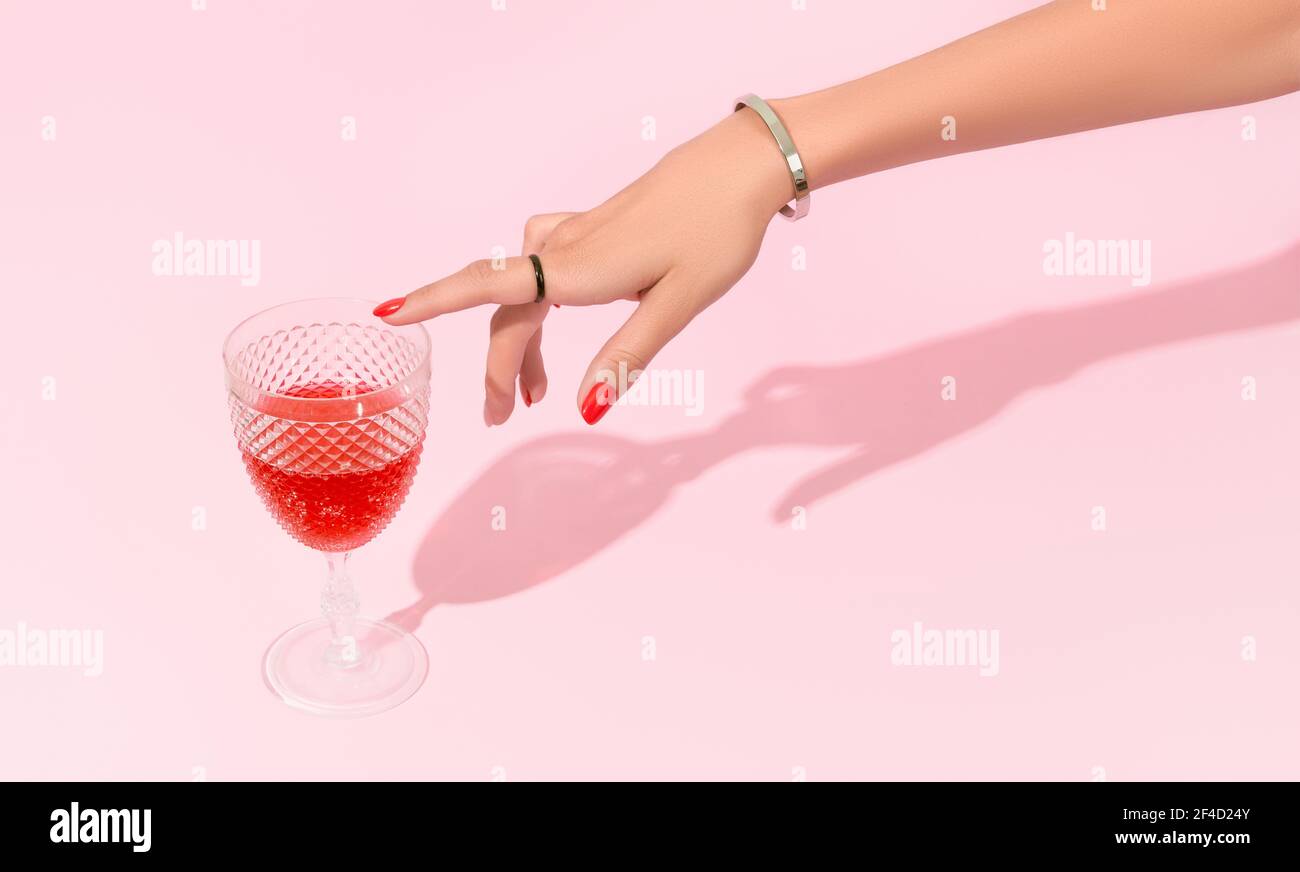 Womans hand touch glass on pink background. Manicure design trends Stock Photo