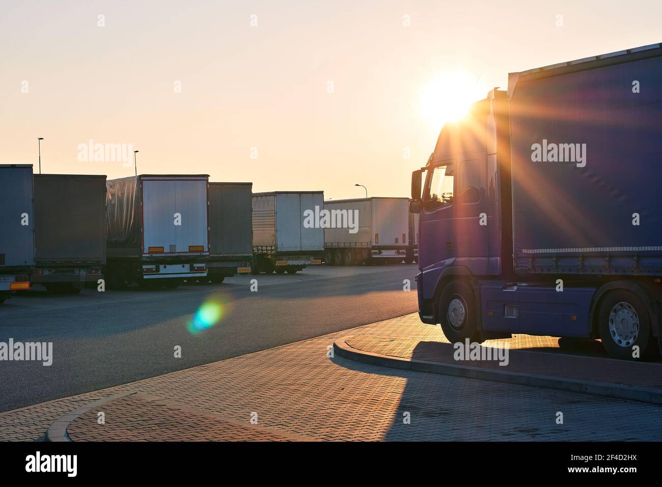 Loaded trucks parked in waiting area on border crossing. Evening view of International hard transportation and logistics with lens flare. Stock Photo