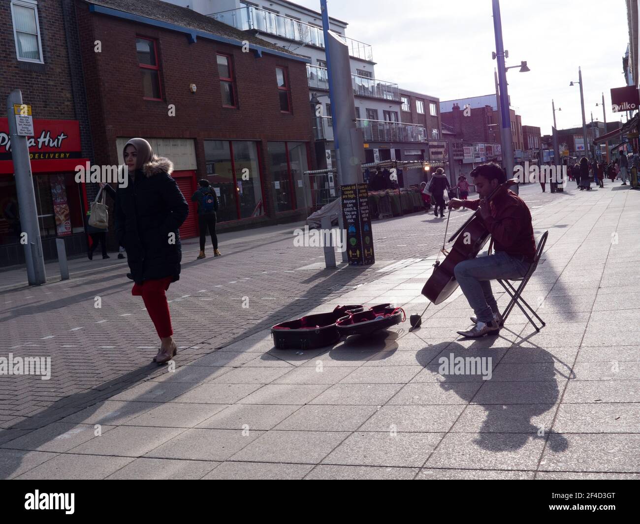 shoppers Walthamstow High Street, Waltham Forest, London with busker playing the cello Stock Photo