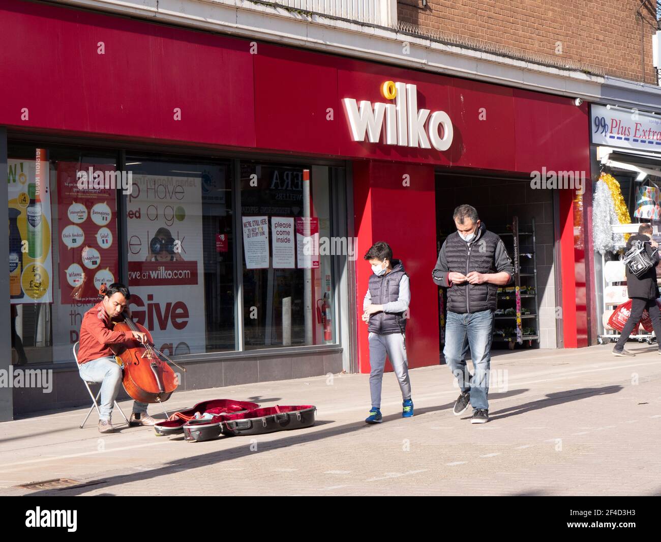 Wilko store shop with shoppers Walthamstow High Street, Waltham Forest, London, with busker playing the cello Stock Photo