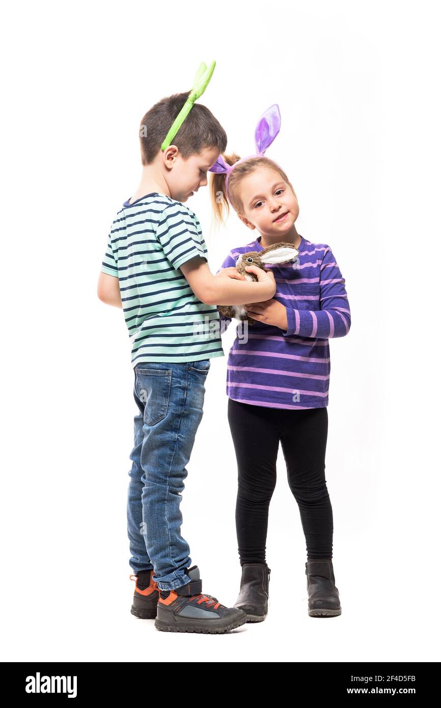 Boy and girl with Easter bunny ears playing with straw rabbit toy. Full ...