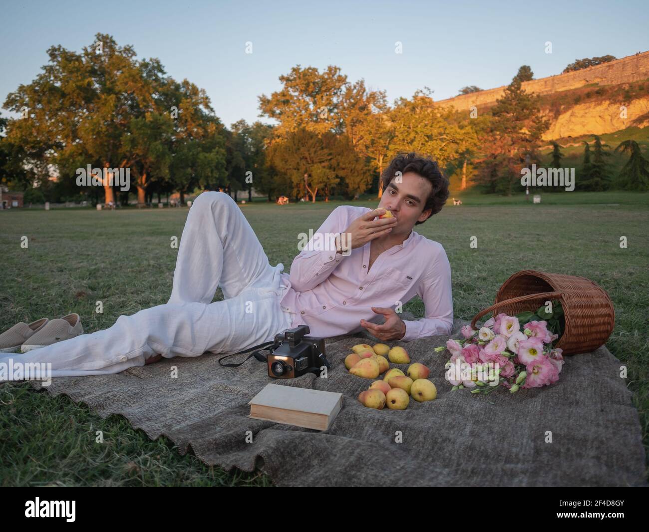 Young man lying on picnic blanket and eating fruit. Relaxing on grass
