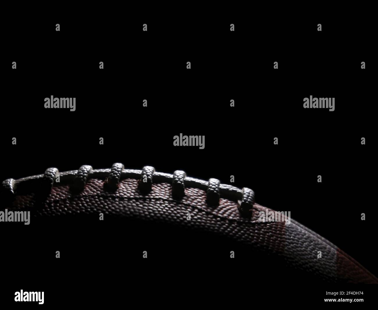 An American football game ball is lit from above from a single light source and set against a black background, with text space above. Stock Photo