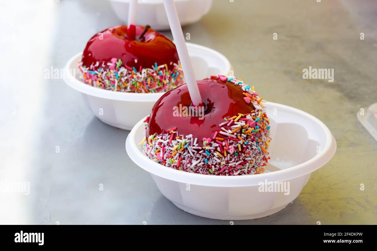 A red caramelized apple on a stick, covered in hard red sugar, standing in a plastic plate to serve as a festive treat. The concept of Easter, Masleni Stock Photo