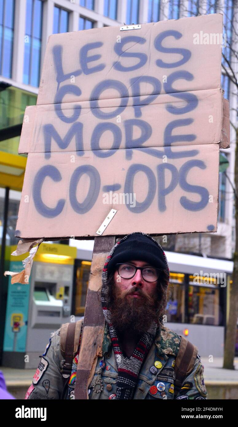 A protester carries a placard: 'Less Cops, More Co-ops'. On March 20, 2021, some 2,000 demonstrators gathered in central Manchester, England, United Kingdom, as three separate demonstrations merged at 4.30pm. They were protesting  about the Police, Crime, Sentencing and Courts Bill, lobbying for more initiatives  to protect the safety of women and demonstrating against the Covid 19 related lockdown measures. This follows the recent murder in London of Sarah Everard. Stock Photo