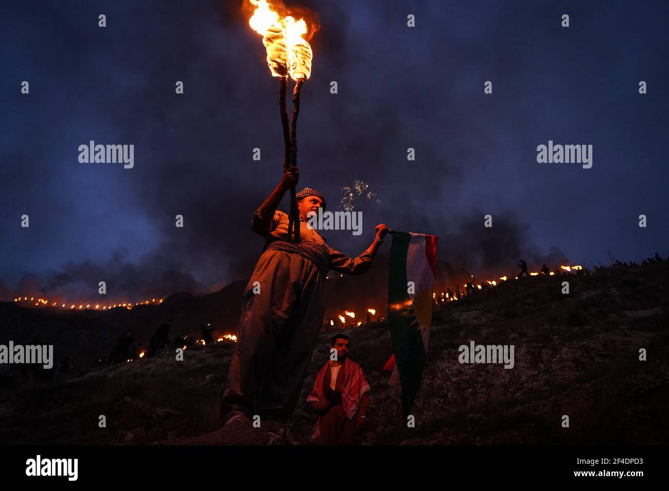 Akre, Iraq. 20th Mar, 2021. A Kurdish man holds a fire torch and a