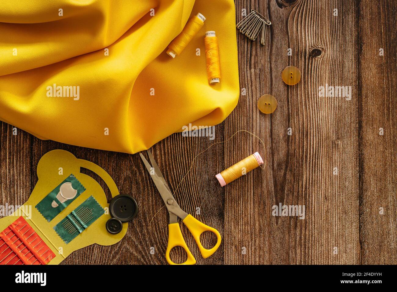 Sewing accessories and yellow fabric on wooden table. Sewing threads, needles, pins, buttons and scissors. Top view, flat lay concept. Accessories Stock Photo