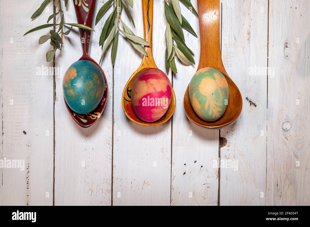 Flatlay Easter composition. Wooden spoons with coloured eggs and olive branches on a shabby chic background. Stock Photo