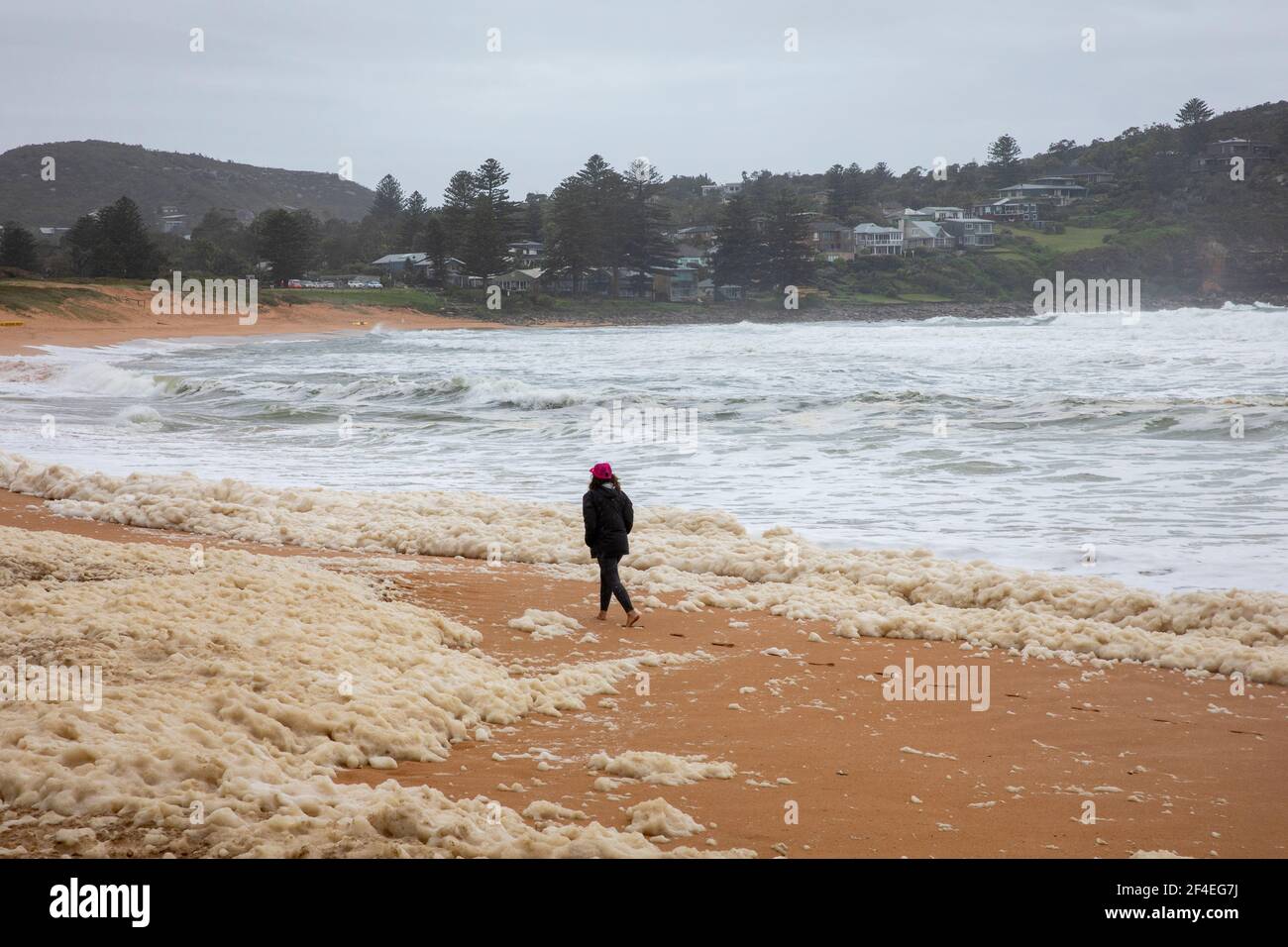 Avalon Beach,Sydney, Australia 21st March 2021.As floods batter New South Wales the east coast surf batters the coastline. Lady walks through the seafoam lying on the beach. Stock Photo