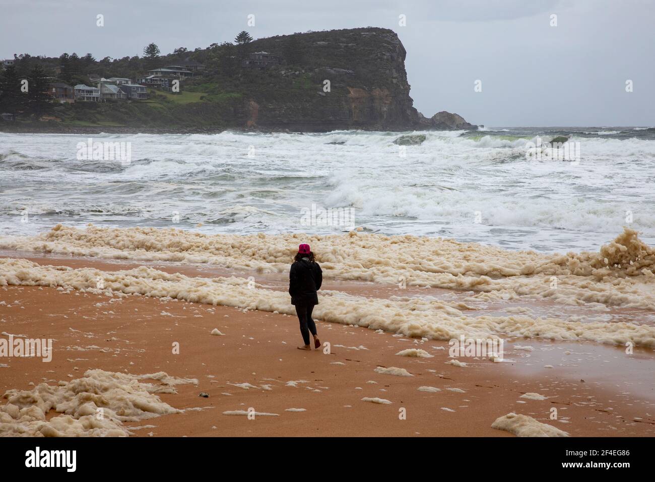 Avalon Beach,Sydney, Australia 21st March 2021.As floods batter New South Wales the east coast surf batters the coastline. Lady walks through the sea foam lying on the beach. Stock Photo