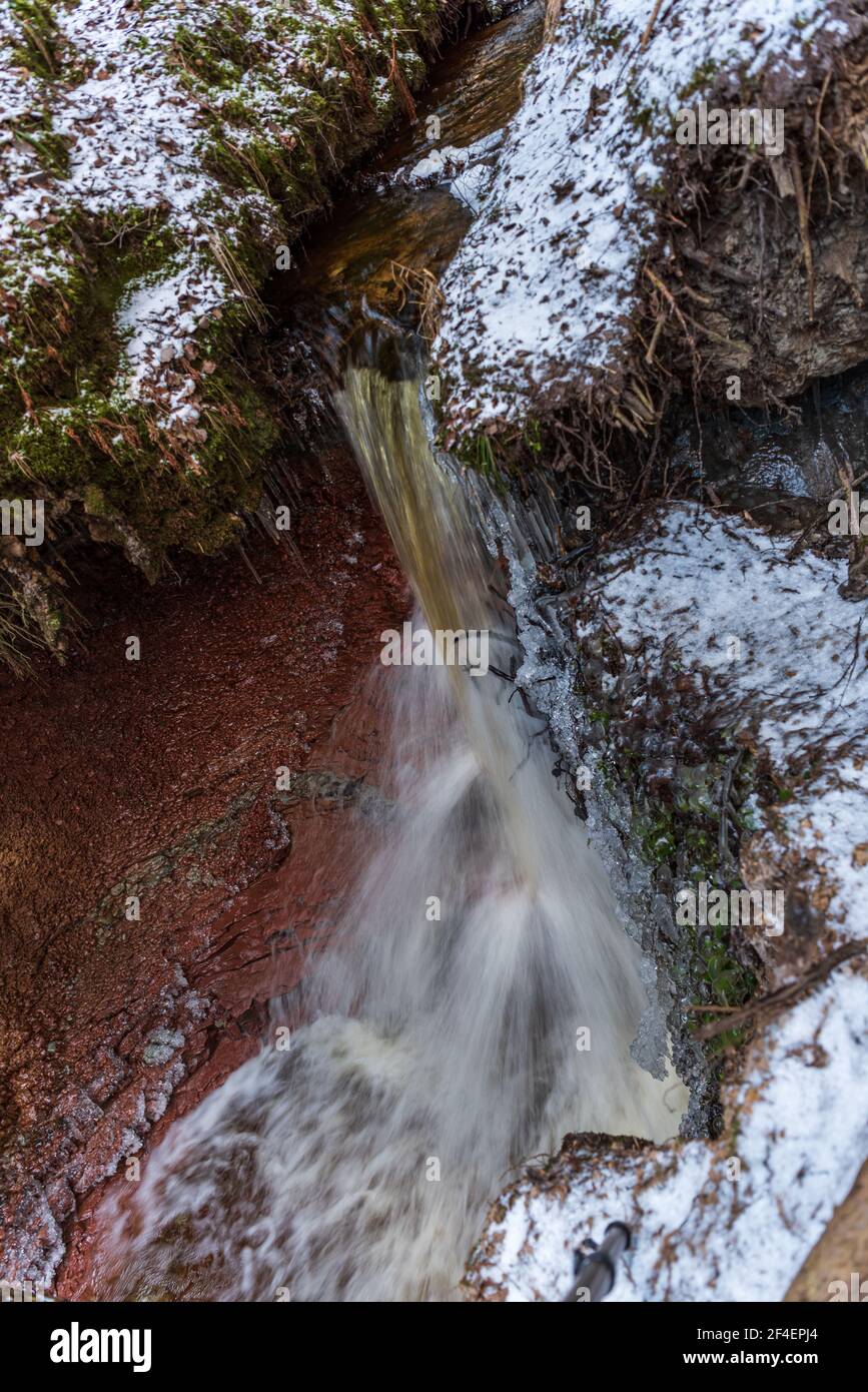 small river waterfall in the forest with a thin layer of snow on the ground and radiant water flow in early spring Stock Photo