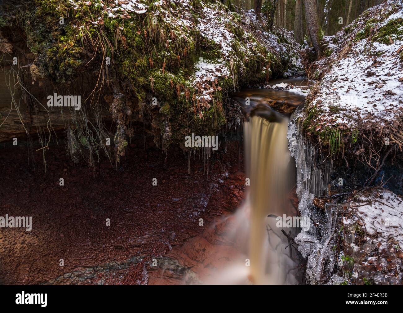small river waterfall in the forest with a thin layer of snow on the ...