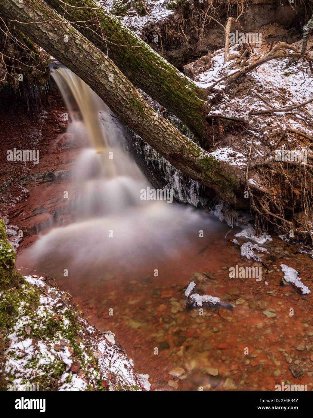 small river waterfall in the forest with a thin layer of snow on the ground and radiant water flow in early spring Stock Photo