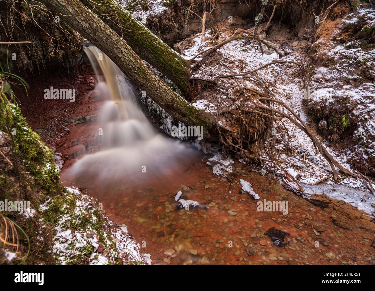 small river waterfall in the forest with a thin layer of snow on the ...