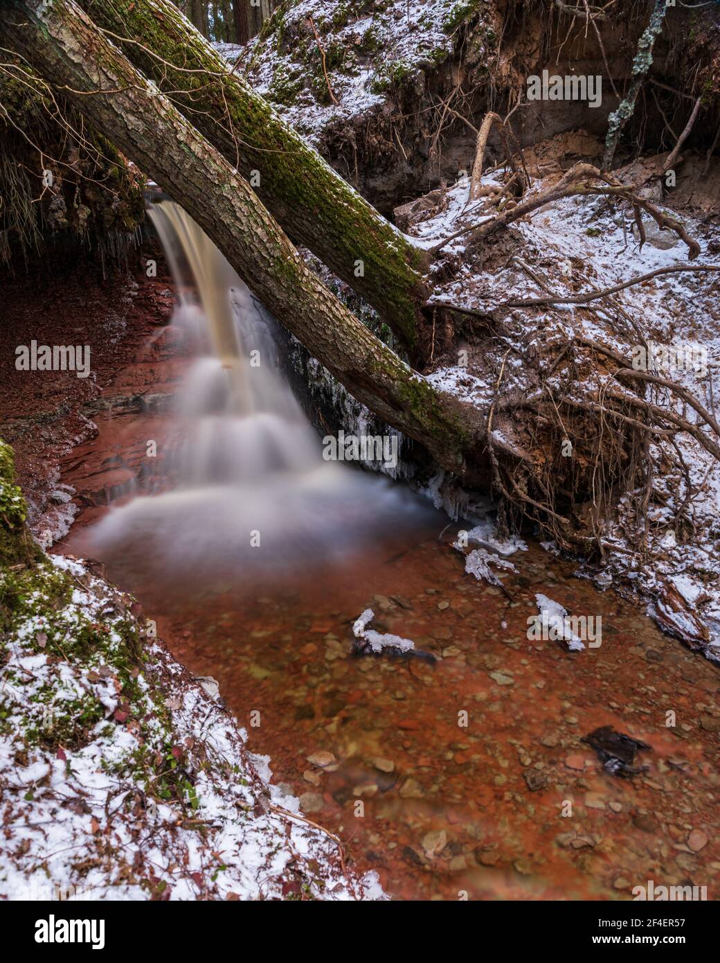 small river waterfall in the forest with a thin layer of snow on the ...