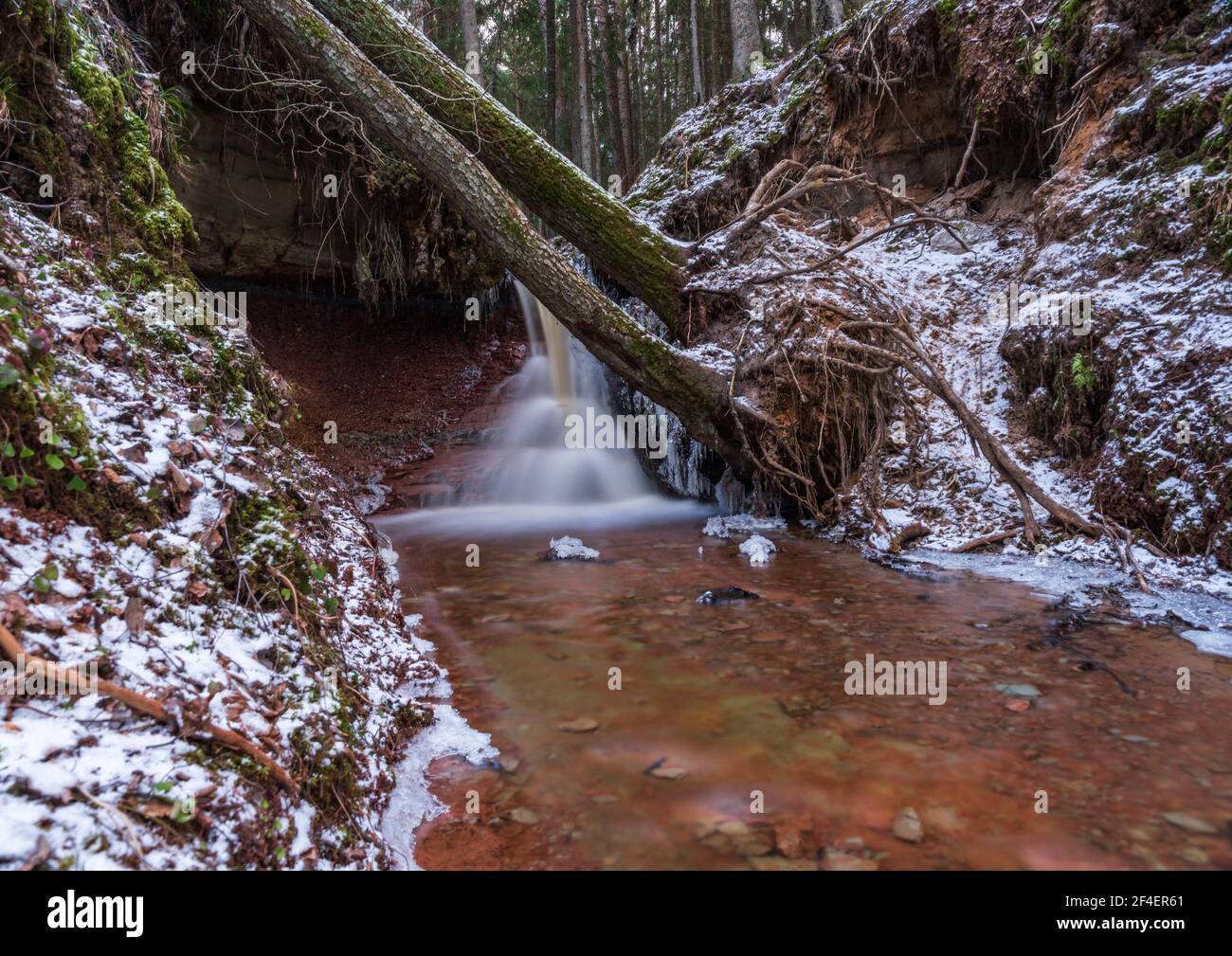 small river waterfall in the forest with a thin layer of snow on the ...