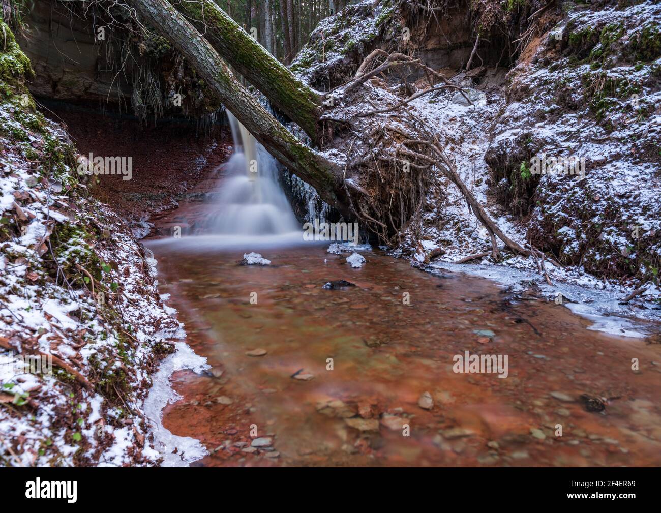 small river waterfall in the forest with a thin layer of snow on the ...