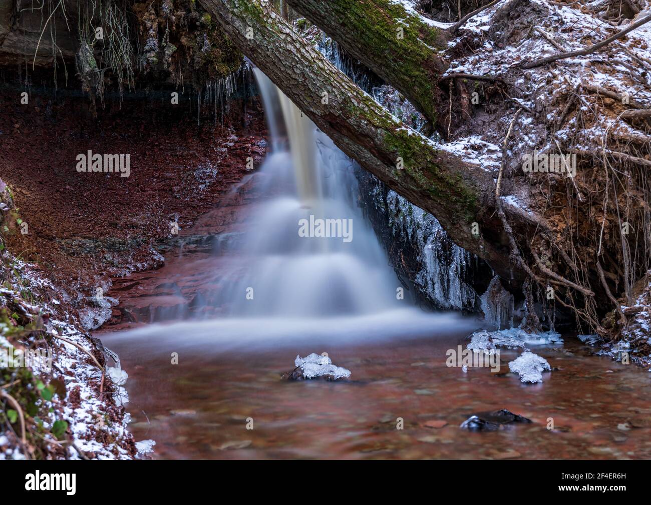 small river waterfall in the forest with a thin layer of snow on the ...