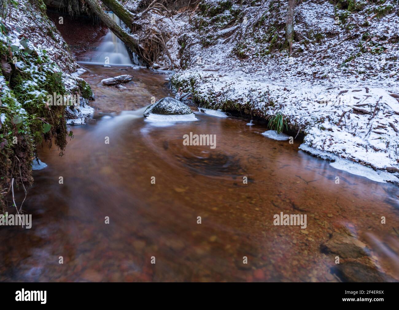 small river waterfall in the forest with a thin layer of snow on the ...