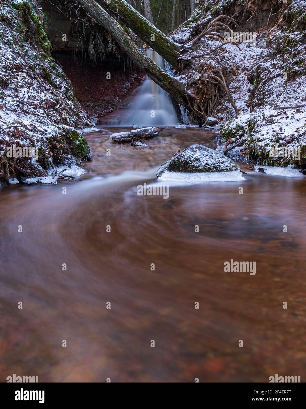 small river waterfall in the forest with a thin layer of snow on the ...