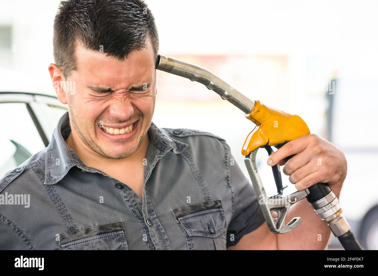 Young man in suicide mimic position at fuel gas station - Gasoline price rising concept with desperate guy pointing pump nozzles pistol on head Stock Photo