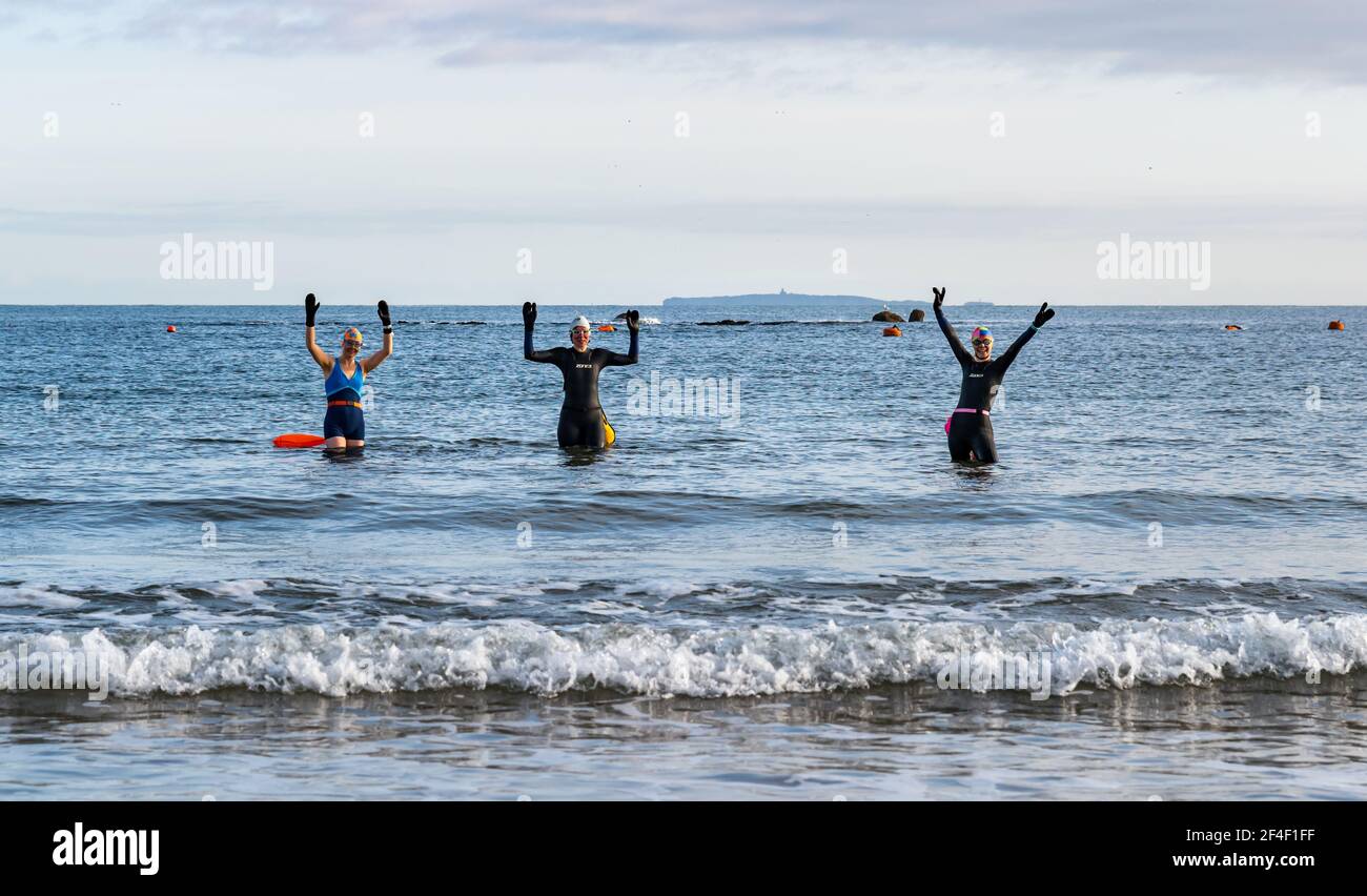 North Berwick, East Lothian, Scotland, United Kingdom, 21st March 2021. UK Weather: wild swimmers go open water swimming in the Firth of Forth. Wild swimming has become a popular sport for locals in the seaside town. These women are some of the regulars who participate in the sport every week throughout the year. Pictured: Alison, Jo and Sarah swim every week, sometimes more often in West Bay, as they enter the sea wearing wetsuits and floats Stock Photo
