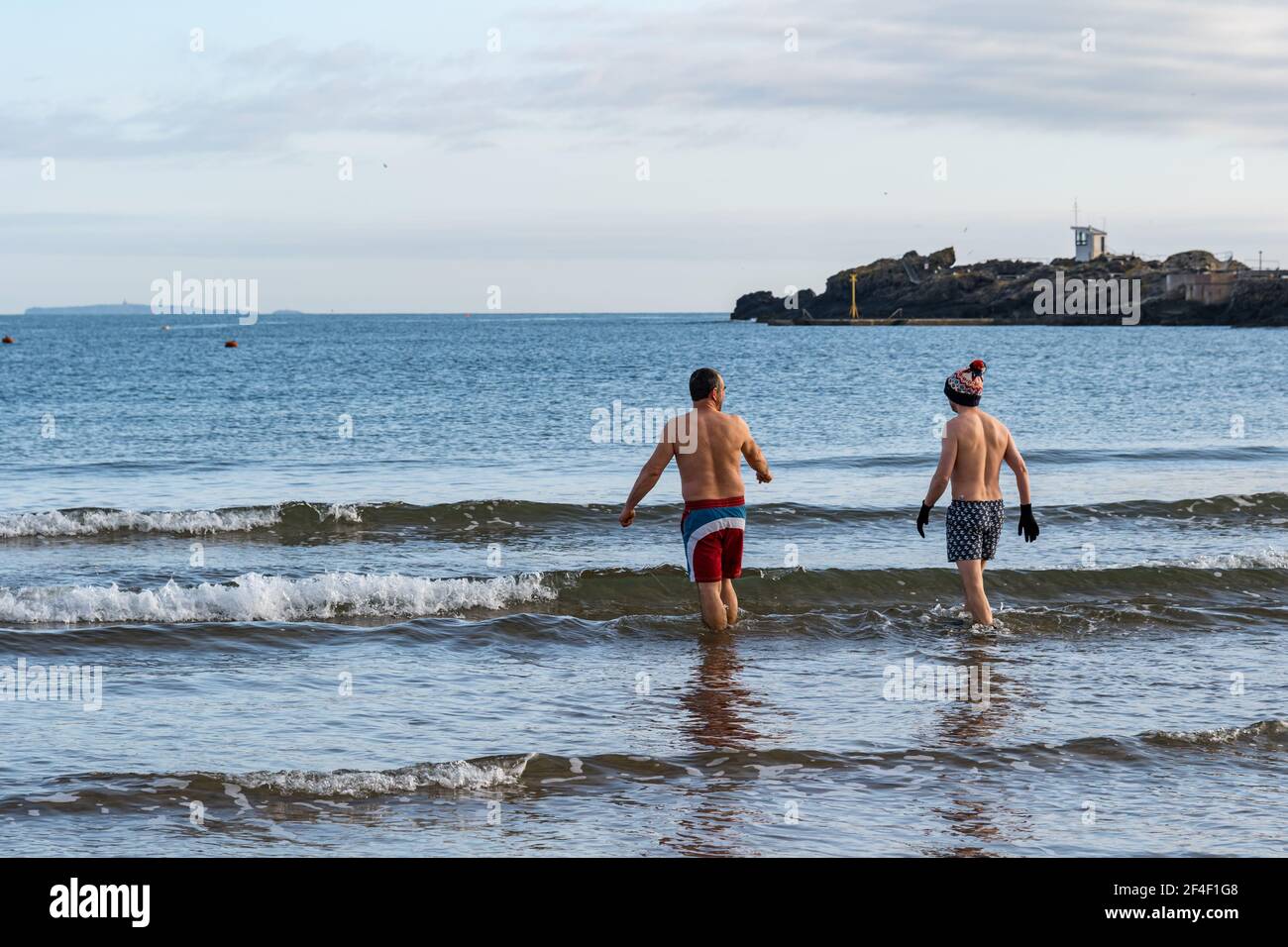North Berwick, East Lothian, Scotland, United Kingdom, 21st March 2021. UK Weather: wild swimmers go open water swimming in the Firth of Forth. Wild swimming has become a popular sport for locals in the seaside town with two men in swimming trunks going into the sea Stock Photo