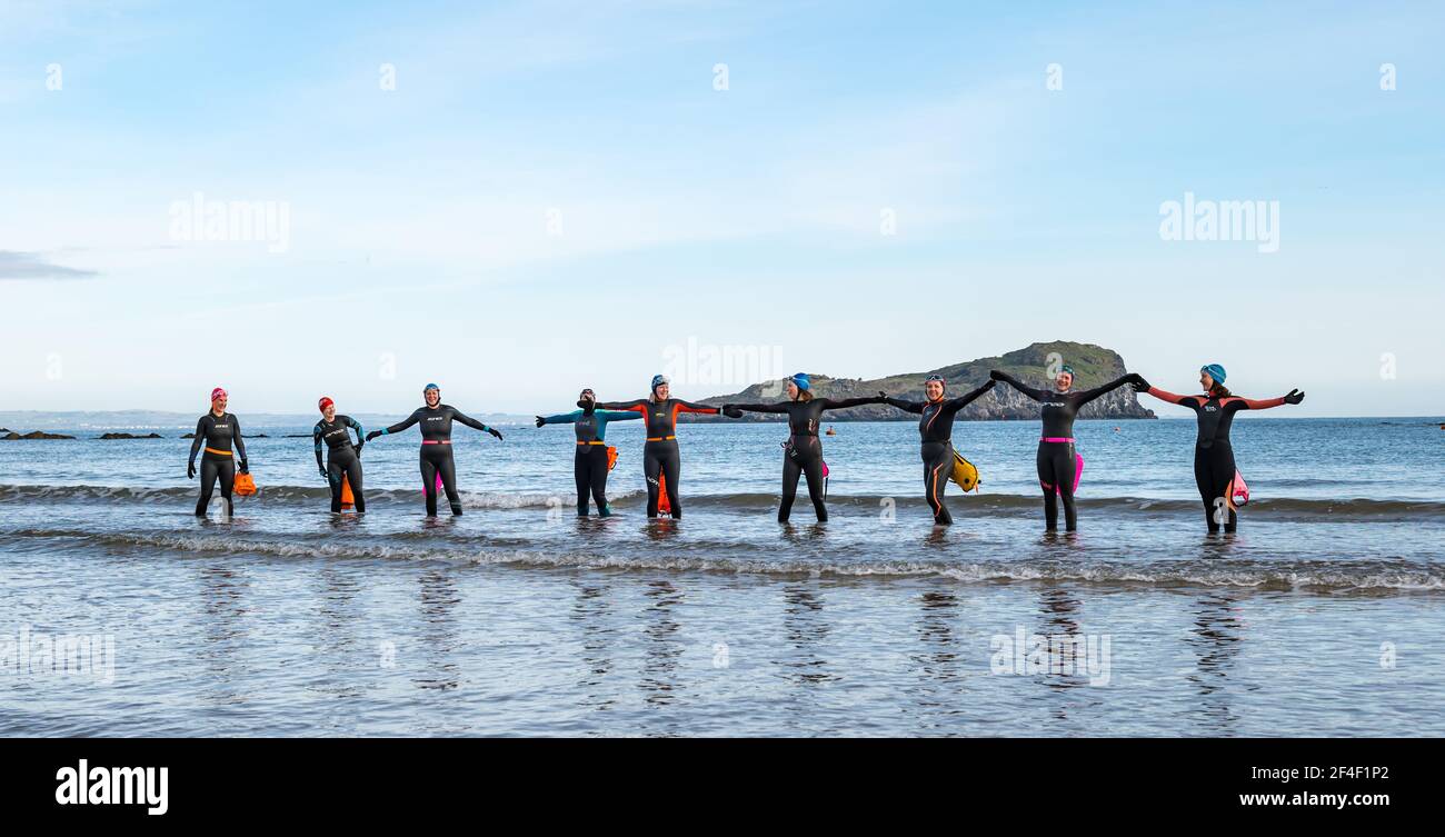 North Berwick, East Lothian, Scotland, United Kingdom, 21st March 2021. UK Weather: wild swimmers go open water swimming in the Firth of Forth. Wild swimming has become a popular sport for locals in the seaside town. These women wearing wetsuits and floats going into the water are some of the regulars who participate in the sport every week throughout the year in West Bay Stock Photo