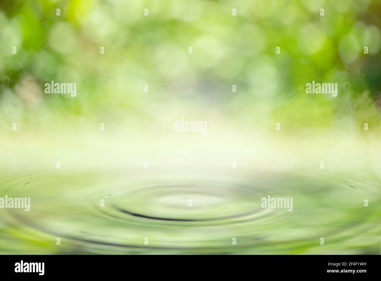 Drop falling in water with ripples with light green bokeh background. Stock Photo