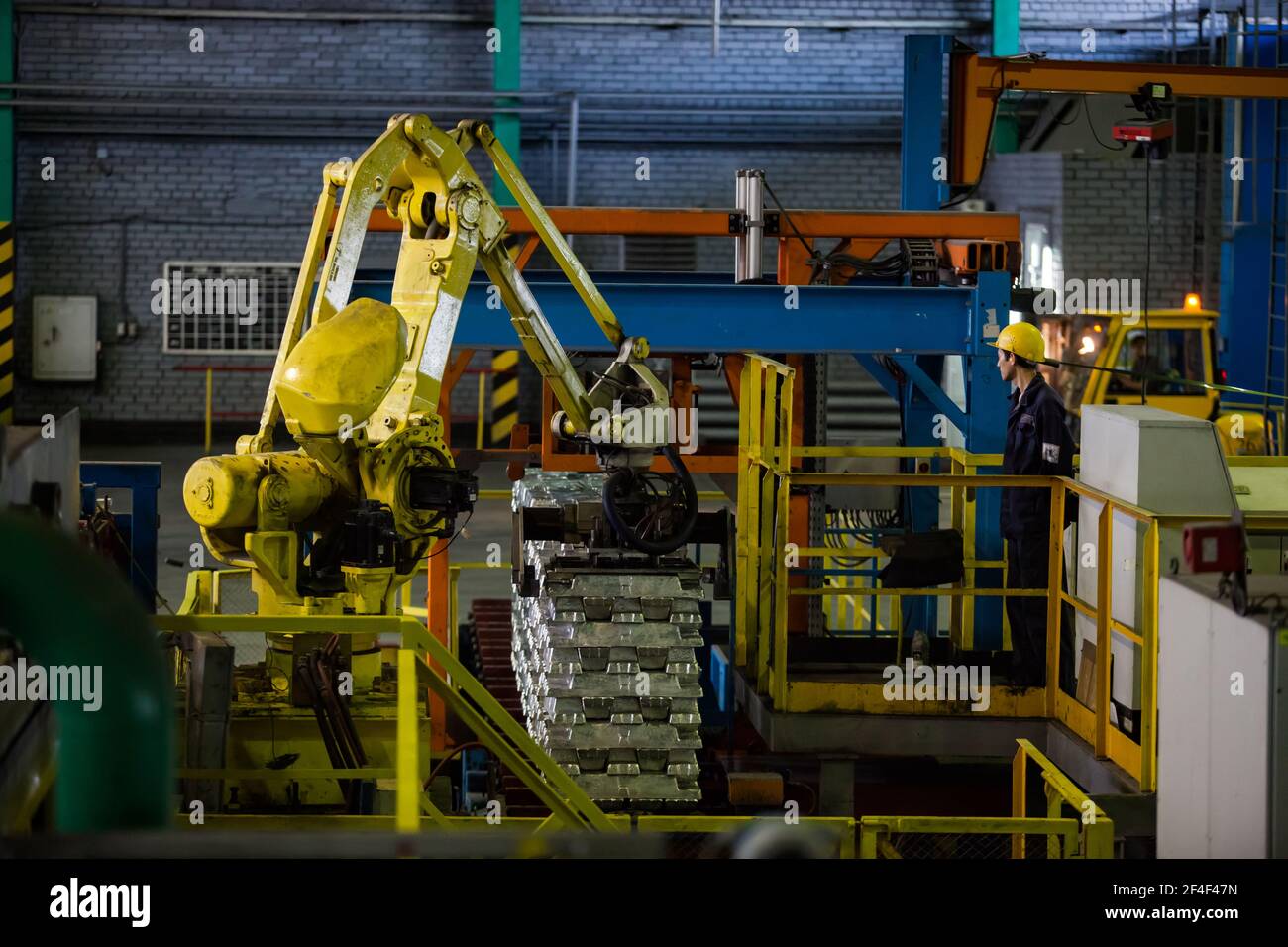 Pavlodar Aluminium electrolysis plant. Aluminium ingots packing machine. Young asian operator worker in yellow hardhat. Stock Photo