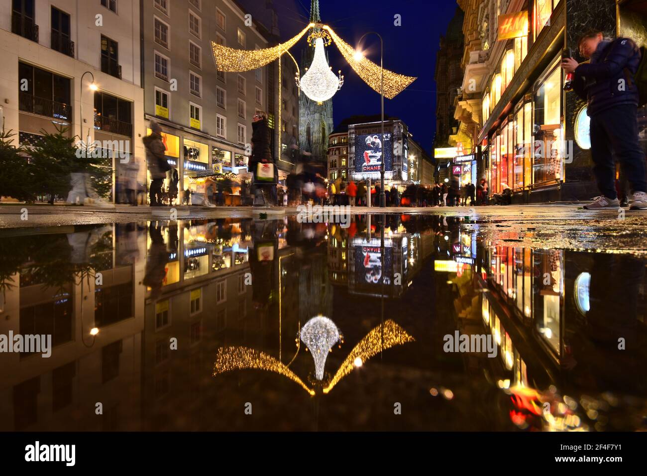 Vienna Graben street in Christmas time reflected in a puddle of water while tourists are sightseeing and shopping. Stock Photo