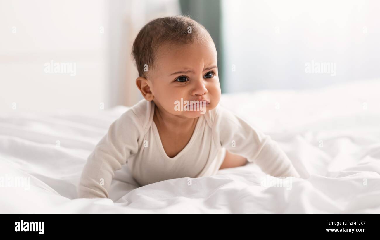 Portrait of sad black baby crying and crawling on bed Stock Photo