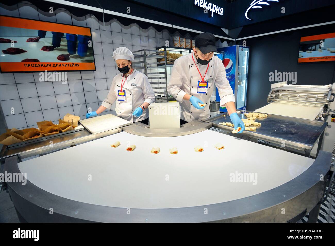 Two bakers making sweet rolls using an automatic bakery production line and dough flattening roller. Mini bakery. March 16, 2021. Berezovka, Ukraine Stock Photo