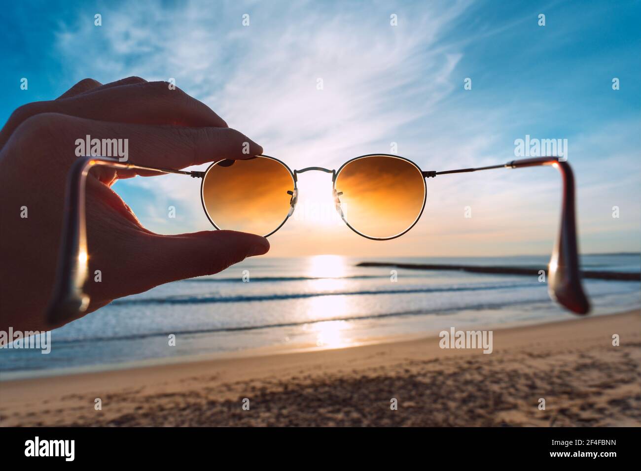 Putting on stylish round polarized sunglasses with brown lenses at sunset Stock Photo