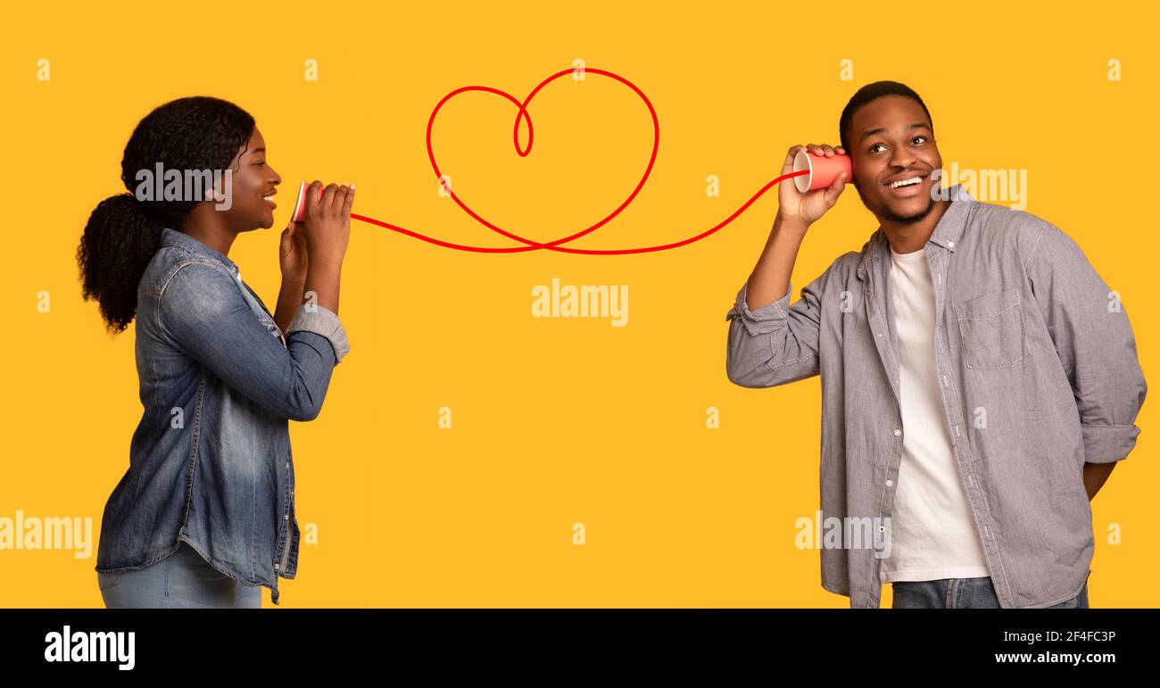 Love Message. Black woman whispering romantic words to boyfriend via tin phone Stock Photo