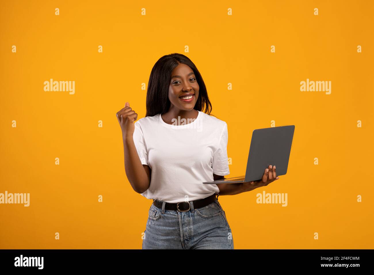 Smiling young black woman holding laptop and raising fist up Stock ...