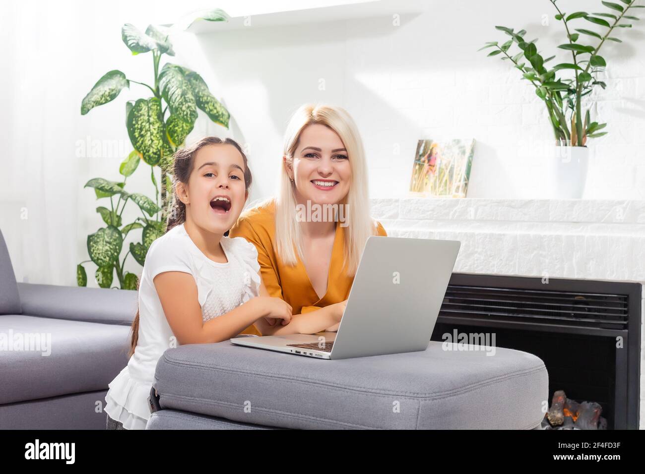 smiling young mother and daughter studying online classes in home