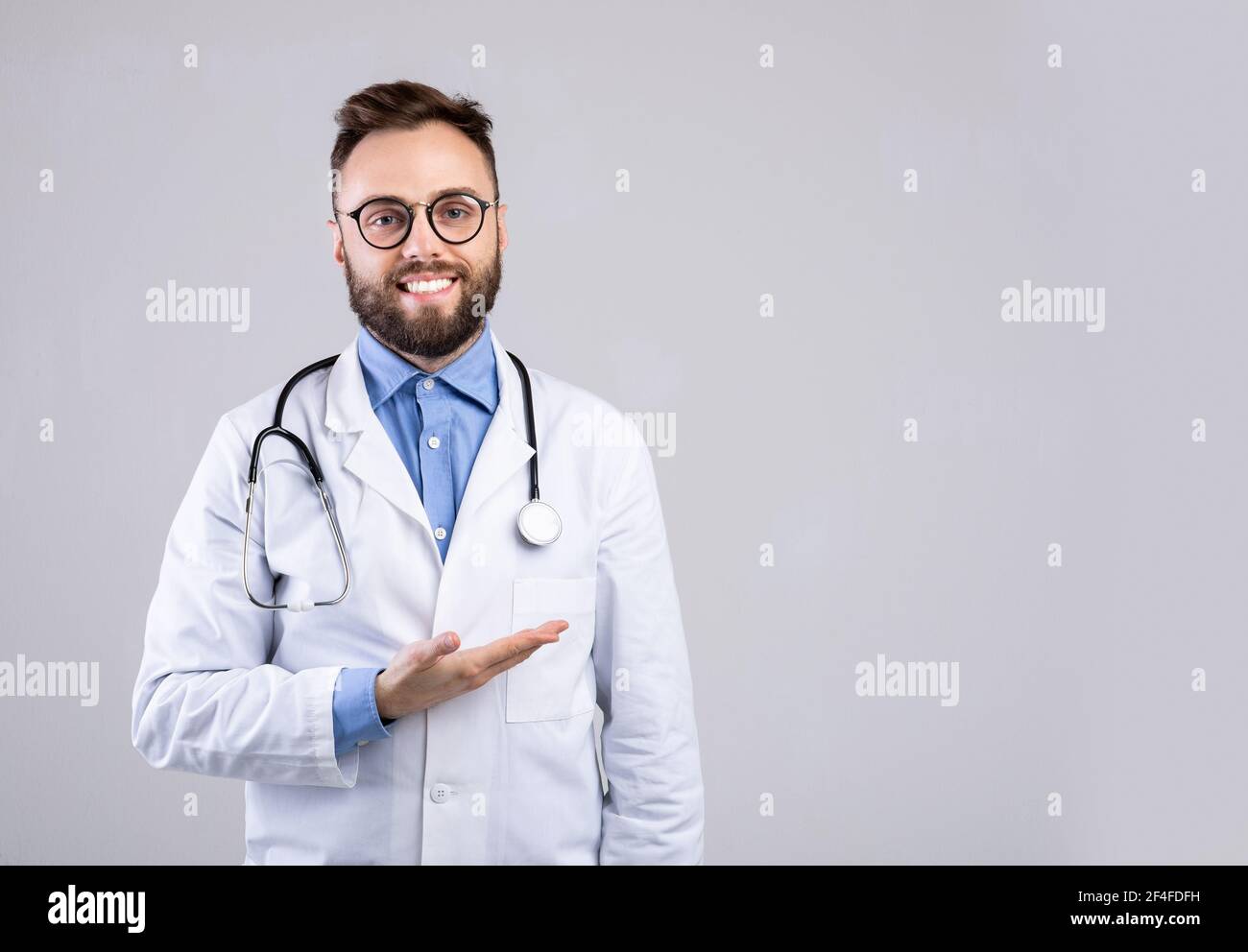 Cheerful male doctor in uniform pointing at empty space over grey studio background, panorama Stock Photo