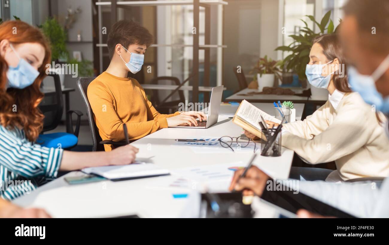 International people wearing surgical masks using laptop sitting in ...