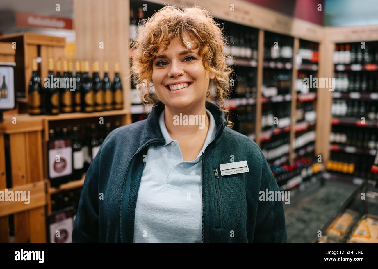 Woman working in a wine store. Portrait of a female connoisseur standing in a liquor store smiling at camera. Stock Photo