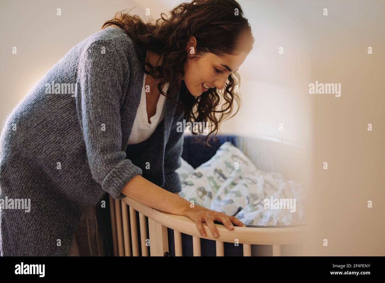 Loving woman putting her baby to sleep in crib. Mother looking after a sleeping baby Stock Photo