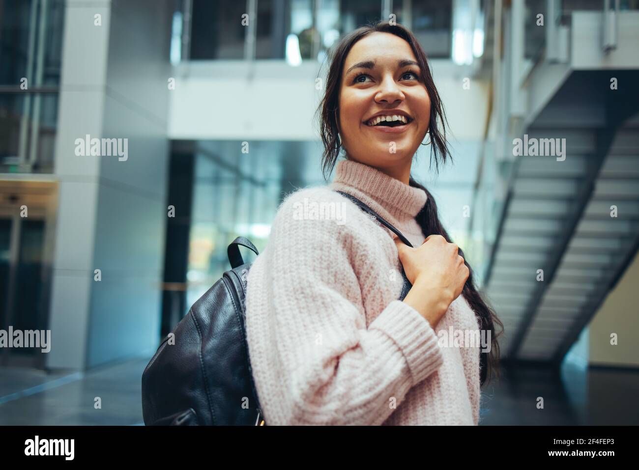 Smiling university student in campus. Happy girl in campus with bag looking over shoulder. Stock Photo