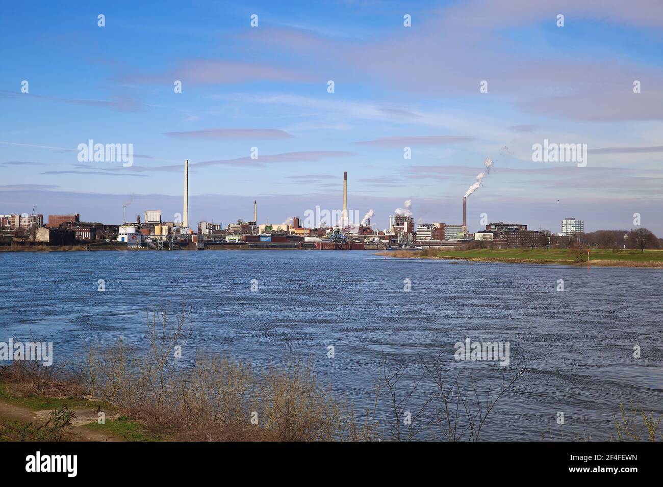 Krefeld (Uerdingen) - March 1. 2021:  View over river rhine on  industrial area with factories and chimneys against blue sky Stock Photo