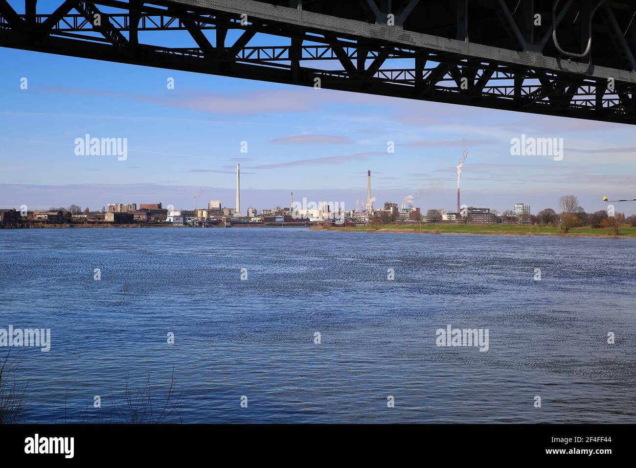 Krefeld (Uerdingen) - March 1. 2021:  View beyond steel bridge over river rhine on  industrial area with factories and chimneys against blue sky Stock Photo