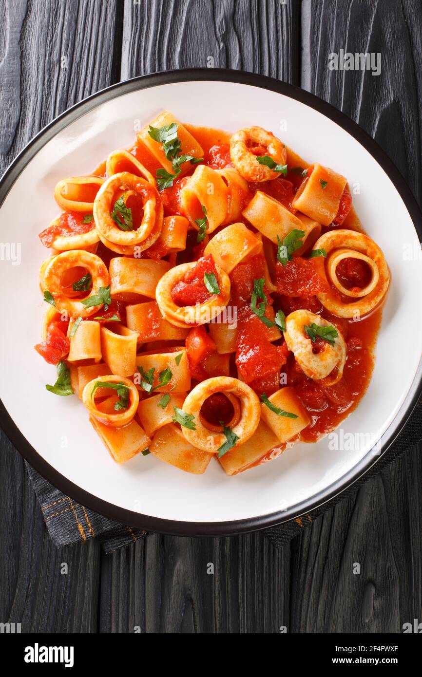 Calamarata pasta with squid in a spicy tomato sauce close-up in a plate on the table. vertical top view from above Stock Photo