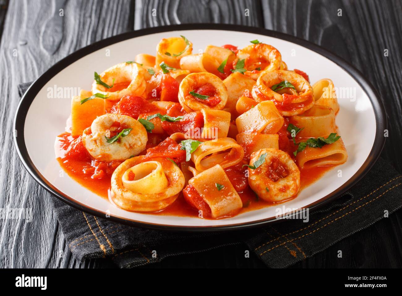 portion of Italian Calamarata pasta with squid rings and tomato close-up in a plate on the table. horizontal Stock Photo