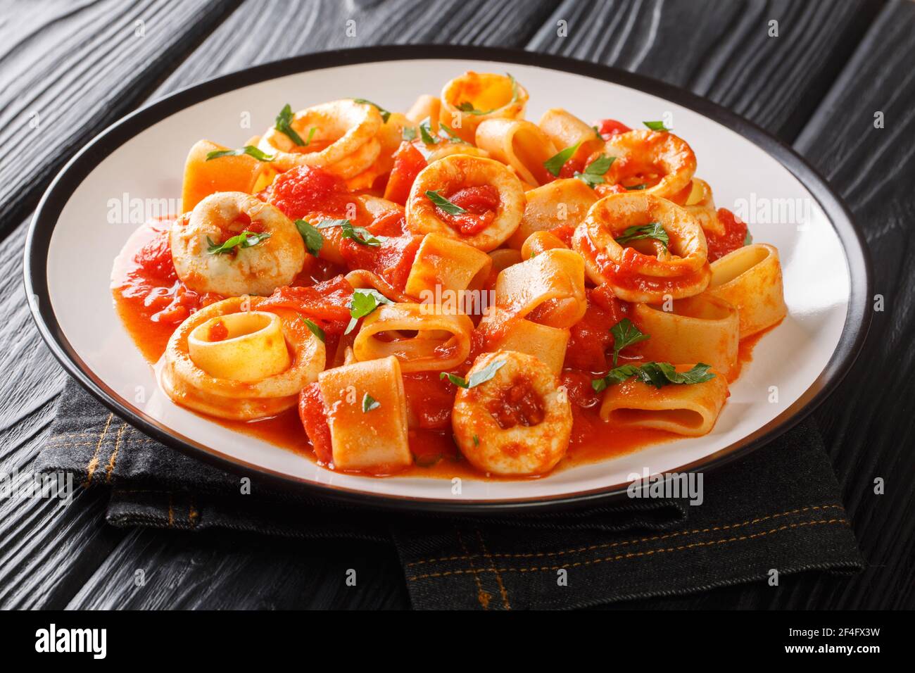 Authentic Italian Calamarata pasta with squid and tomato close-up in a plate on the table. horizontal Stock Photo