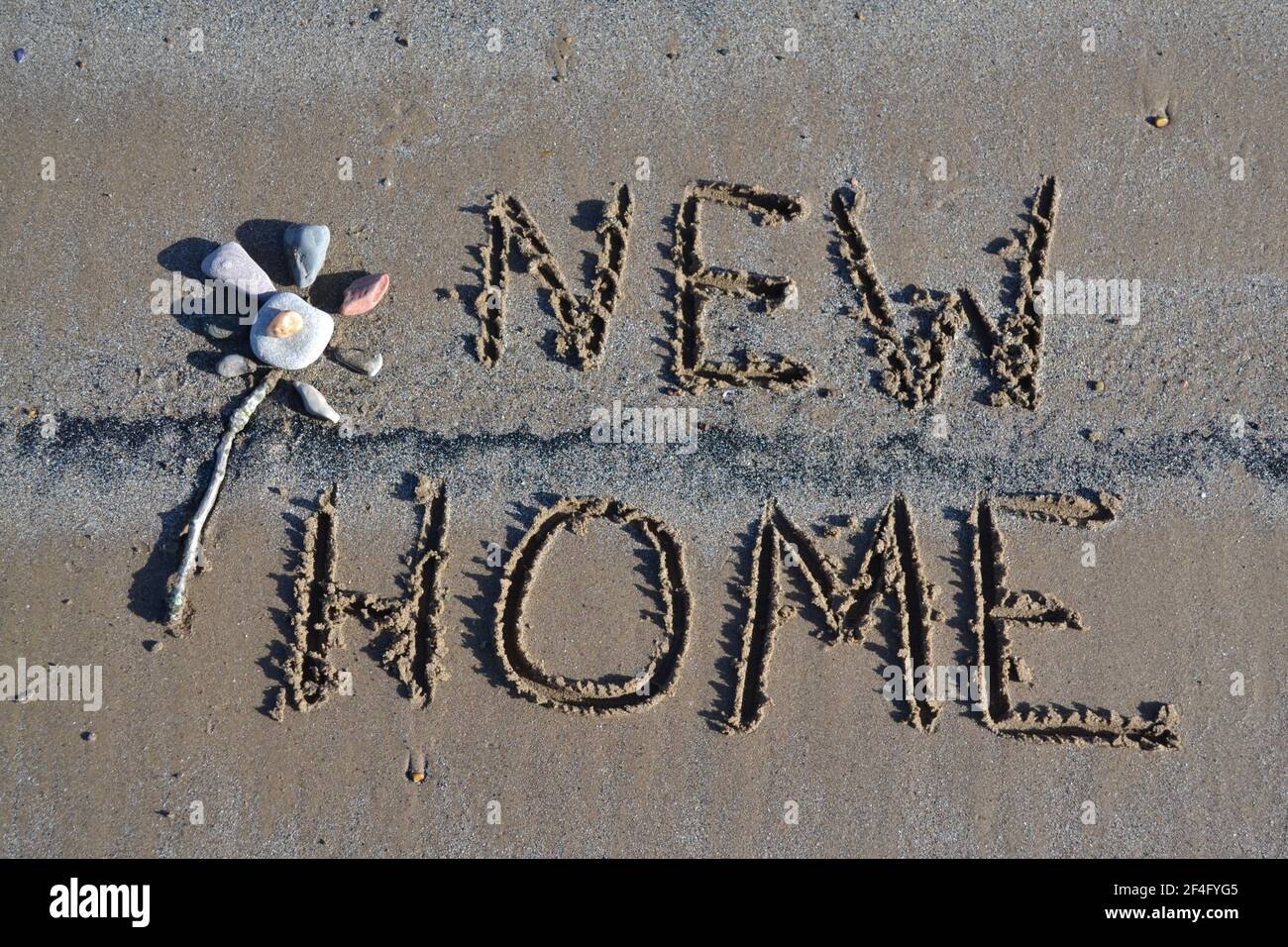 New Home Written In The Sand On Filey Beach - Stone Art - Flower Stone Art - Sunny Day On A Sandy Beach In Yorkshire UK Stock Photo